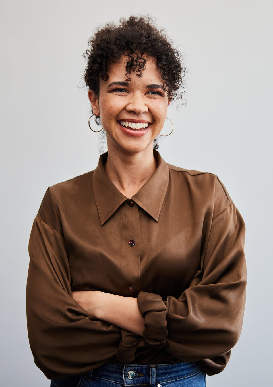 Portrait of a young businesswoman smiling while standing with her arms crossed in front of a white wall in an office